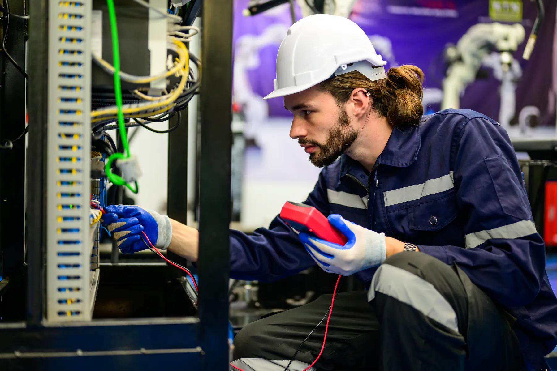 Elektryk w kasku sprawdza miernikiem okablowanie w szafie sterowniczej