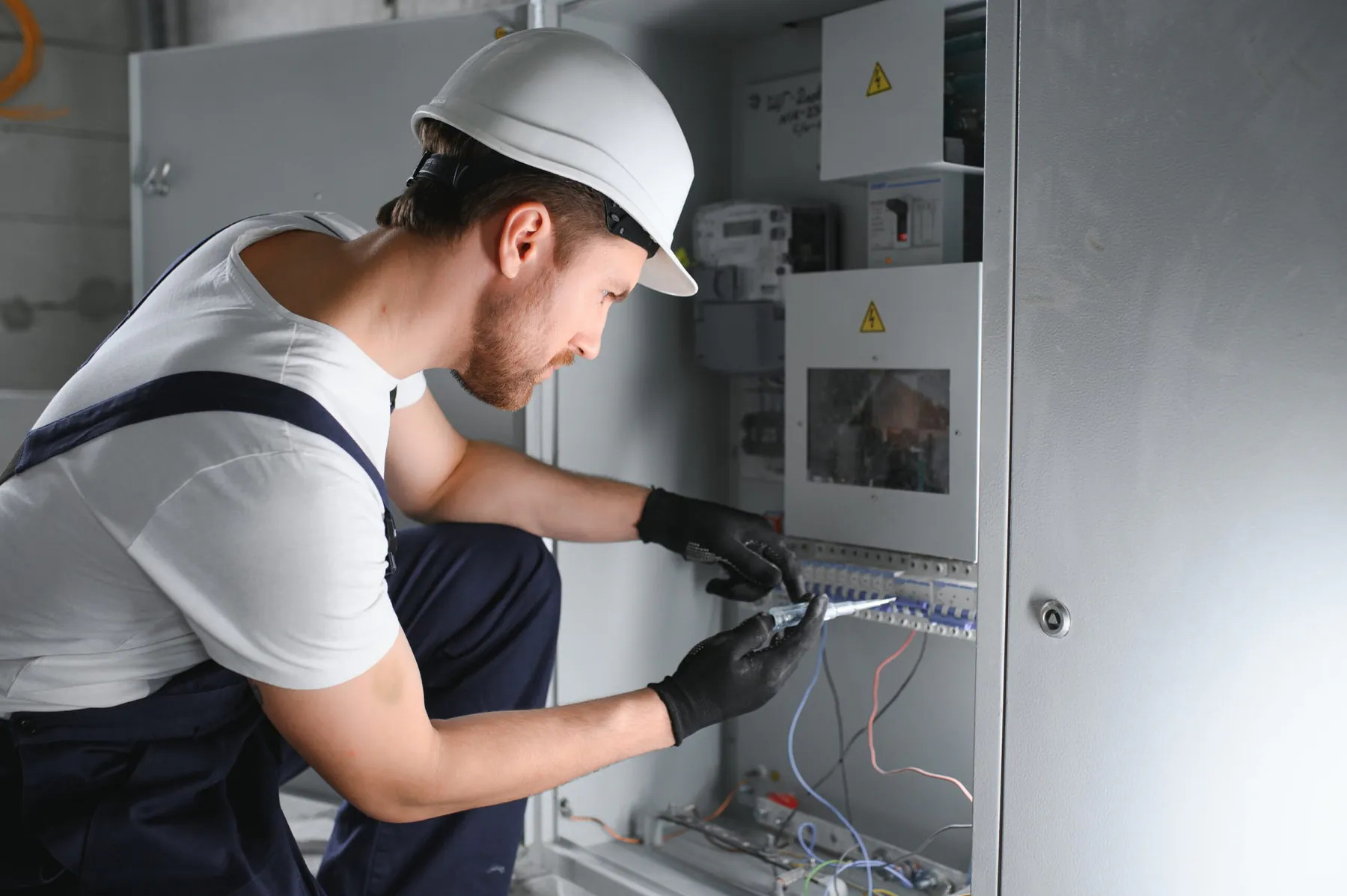 Elektryk w kasku sprawdza próbnikiem napięcia zabezpieczenia w rozdzielnicy